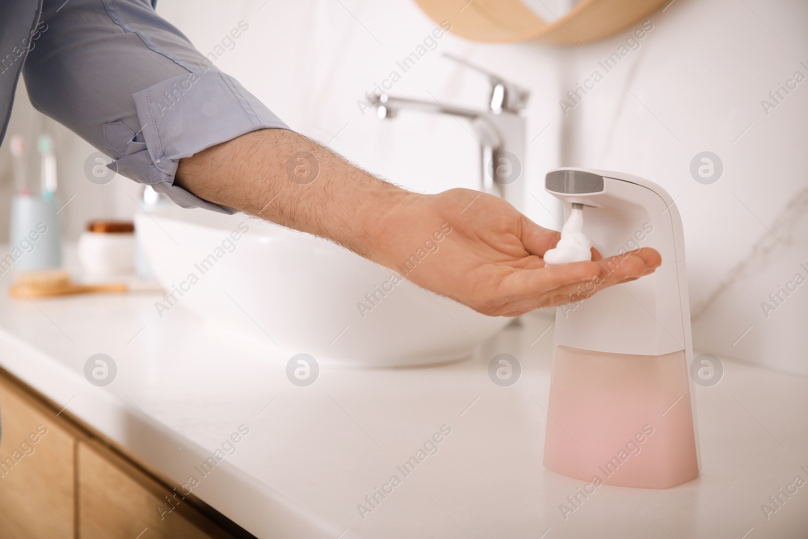 Photo of Man using automatic soap dispenser in bathroom, closeup