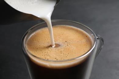 Photo of Pouring milk into cup of coffee on black table, closeup
