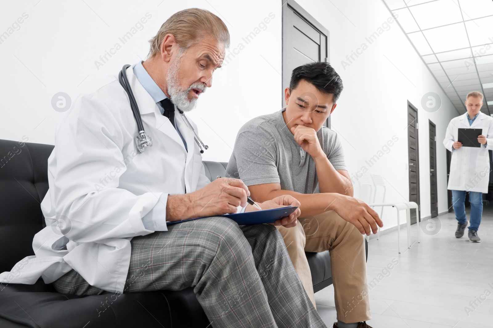 Photo of Senior doctor with clipboard consulting patient in clinic