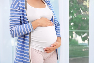 Young pregnant woman near window at home, closeup