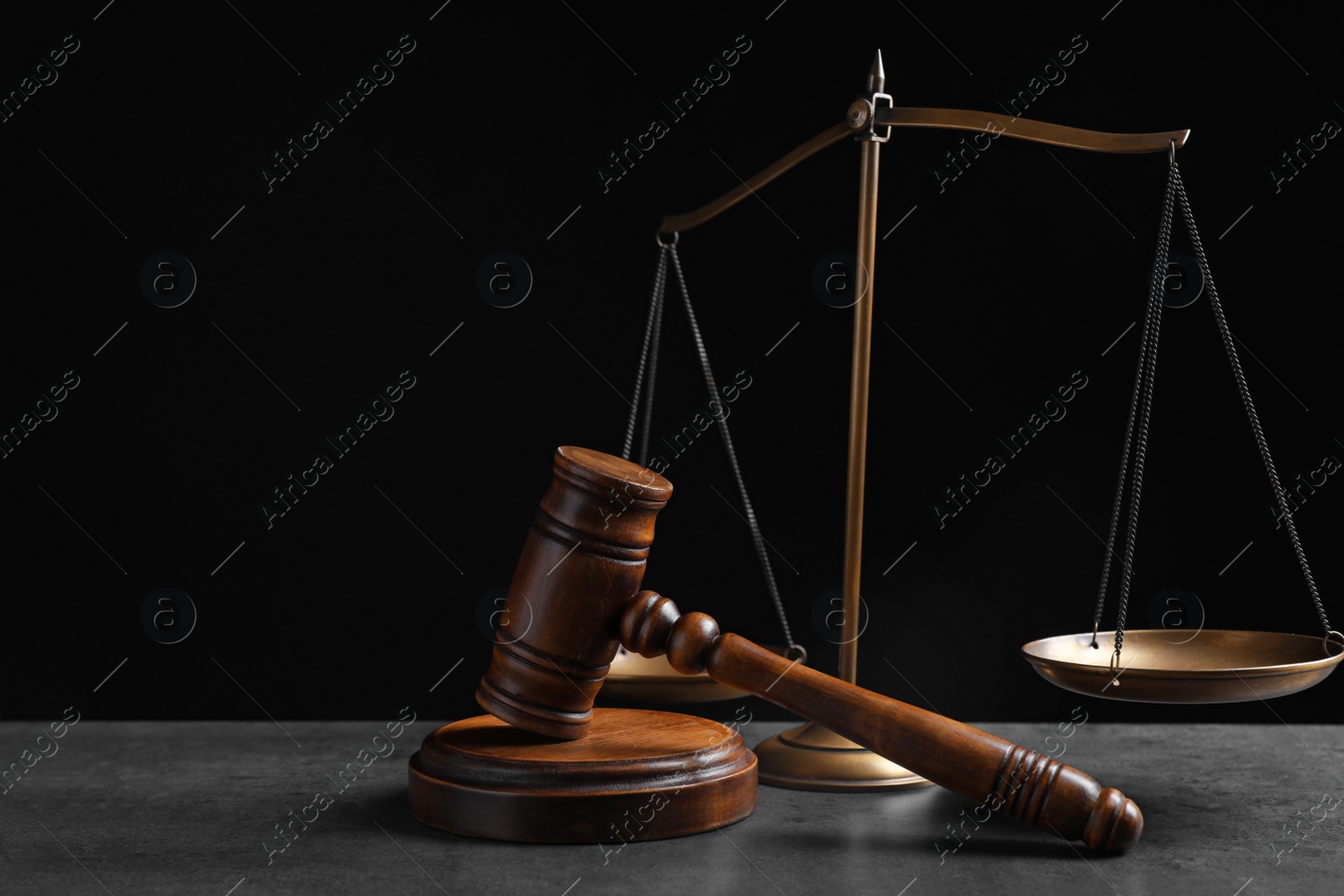 Photo of Judge's gavel and scales on grey table against black background. Criminal law concept