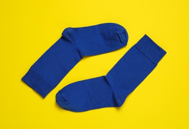 Photo of Pair of new blue socks on yellow background, flat lay