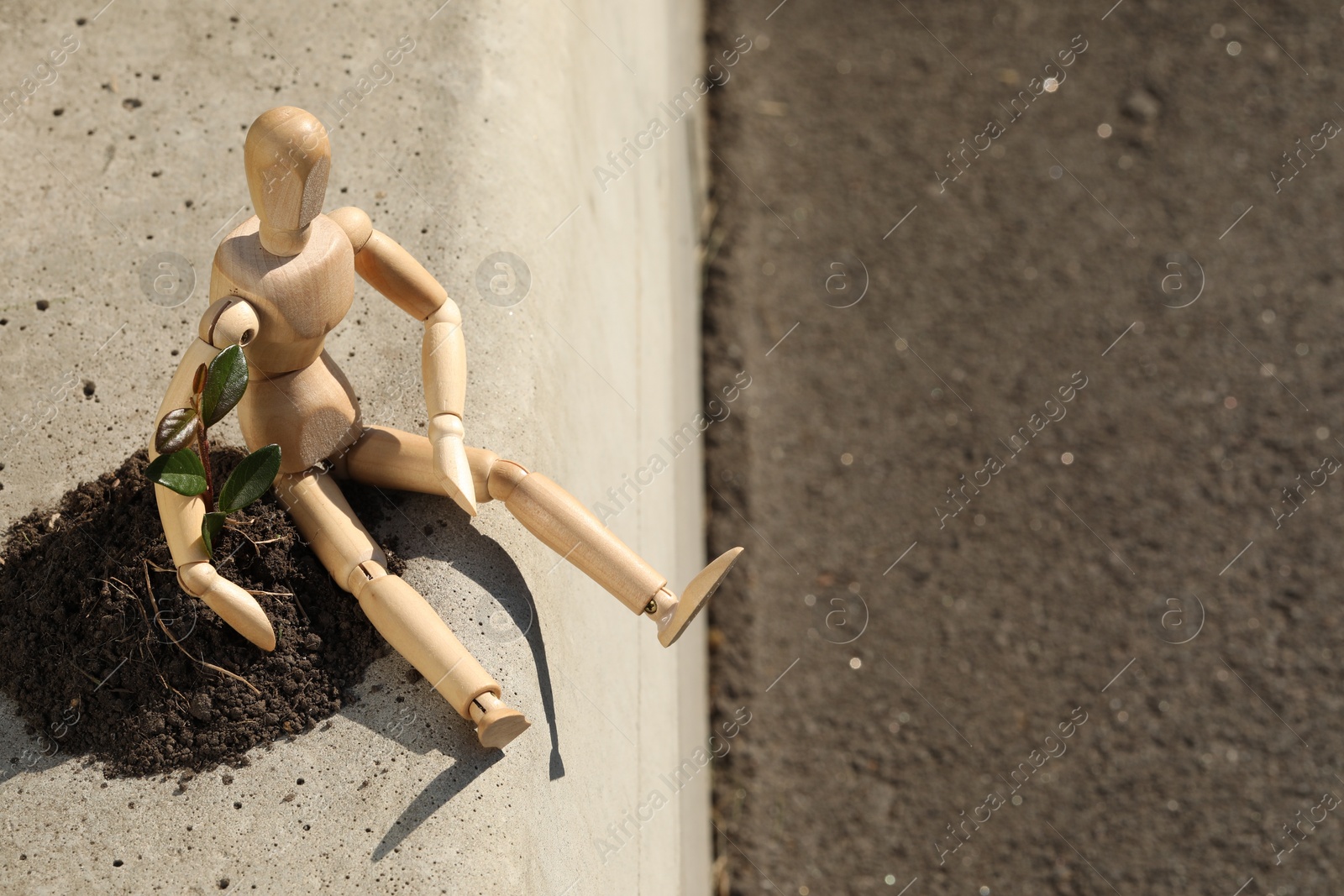 Photo of Wooden human figure with soil and green seedling outdoors, space for text