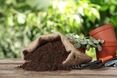 Photo of Bag of soil and gardening equipment on wooden table against blurred background, space for text