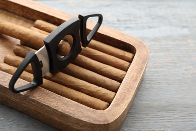 Photo of Many cigars and cutter in box on grey wooden table, closeup