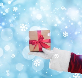 Image of Santa Claus holding gift box on winter background, bokeh effect