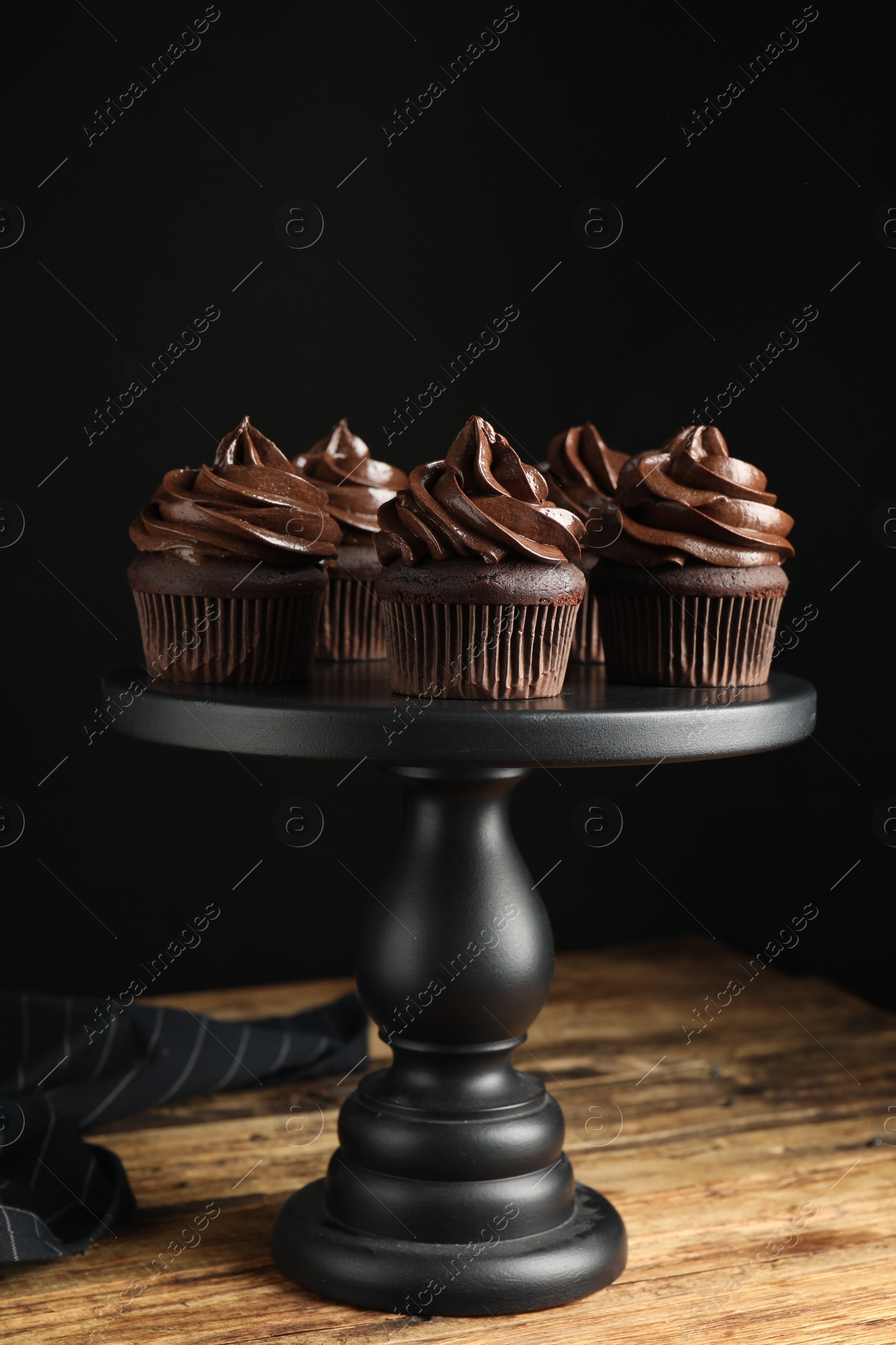 Photo of Dessert stand with delicious chocolate cupcakes on wooden table against black background