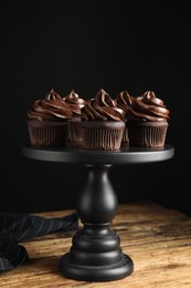 Dessert stand with delicious chocolate cupcakes on wooden table against black background