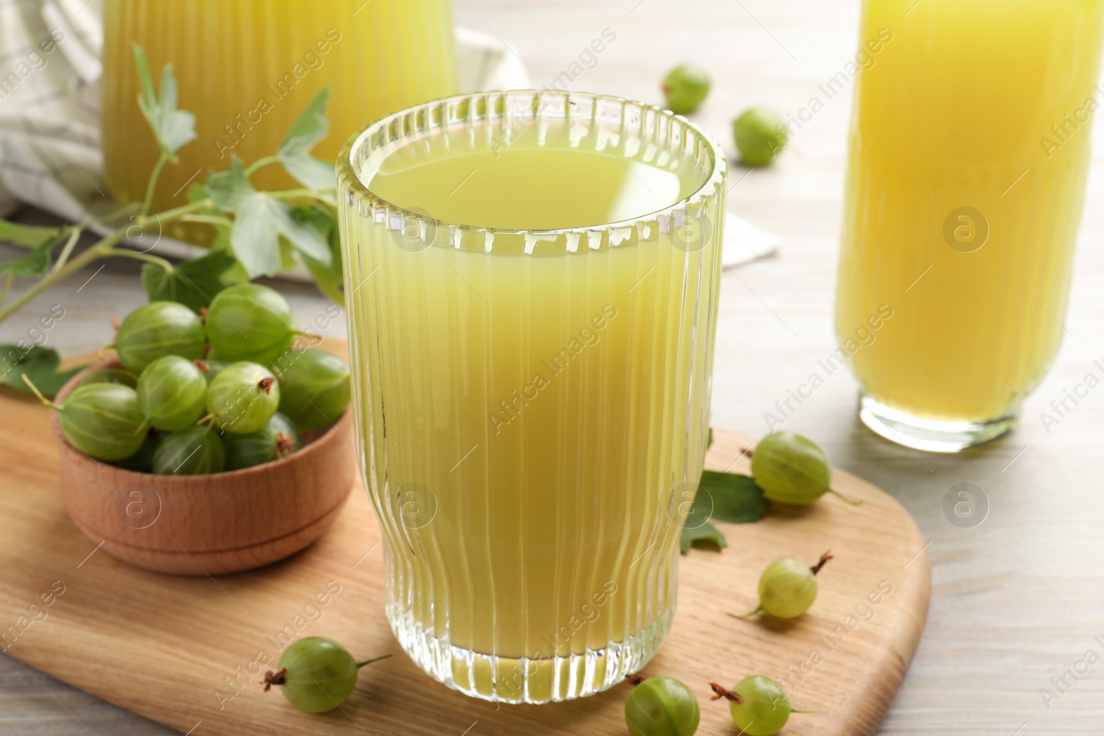 Photo of Tasty gooseberry juice and fresh berries on light wooden table