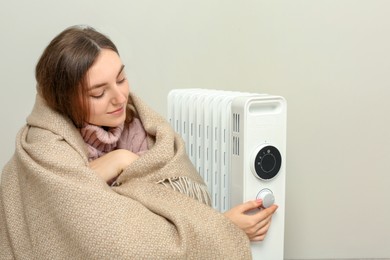 Photo of Young woman adjusting temperature on modern electric heater near beige wall