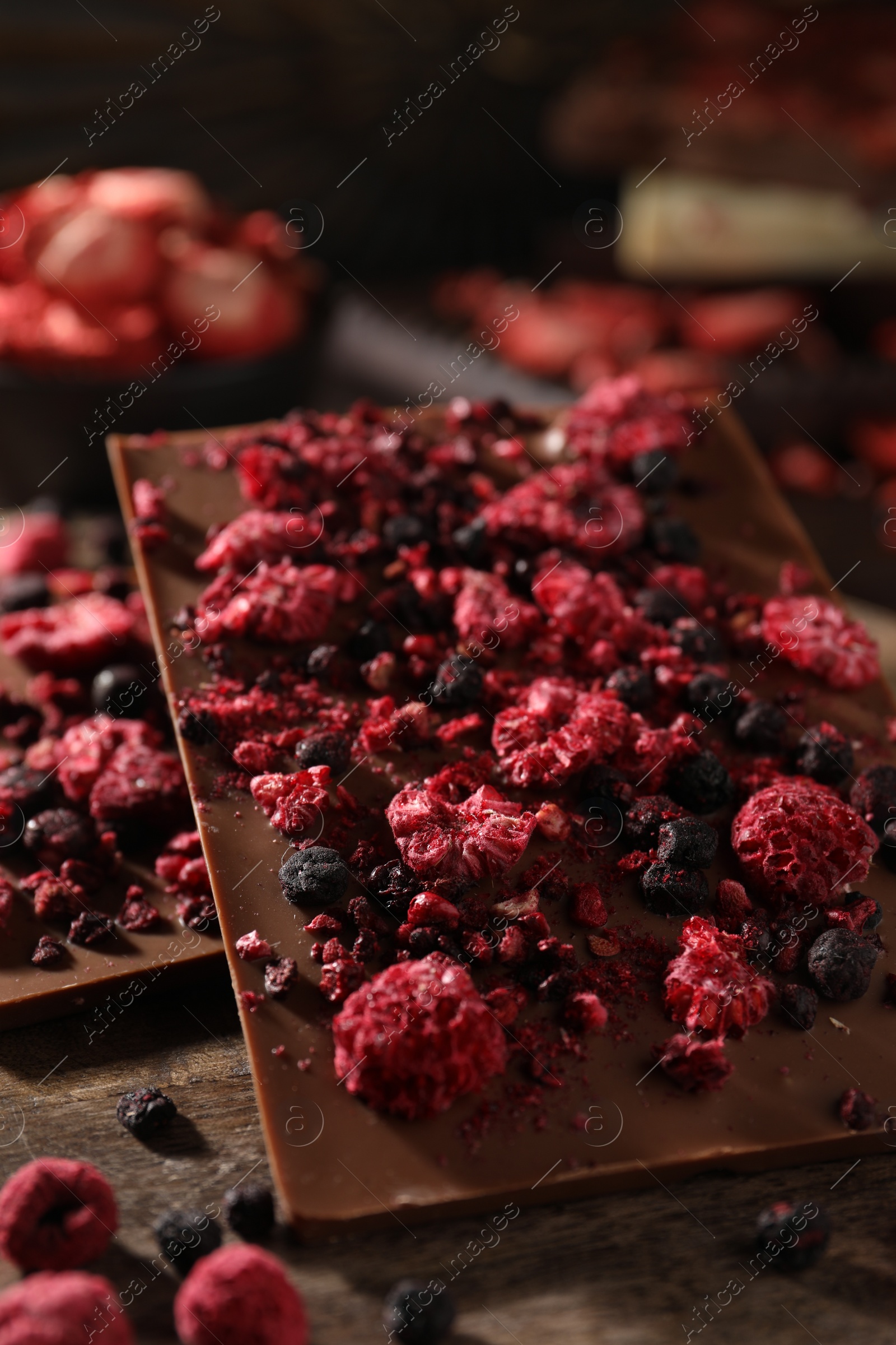 Photo of Chocolate bars with different freeze dried fruits on wooden board, closeup