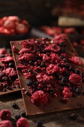 Chocolate bars with different freeze dried fruits on wooden board, closeup