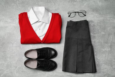 Photo of Stylish school uniform for girl and glasses on grey background, flat lay