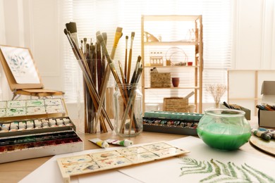 Photo of Different brushes and paints on wooden table in studio. Artist's workplace