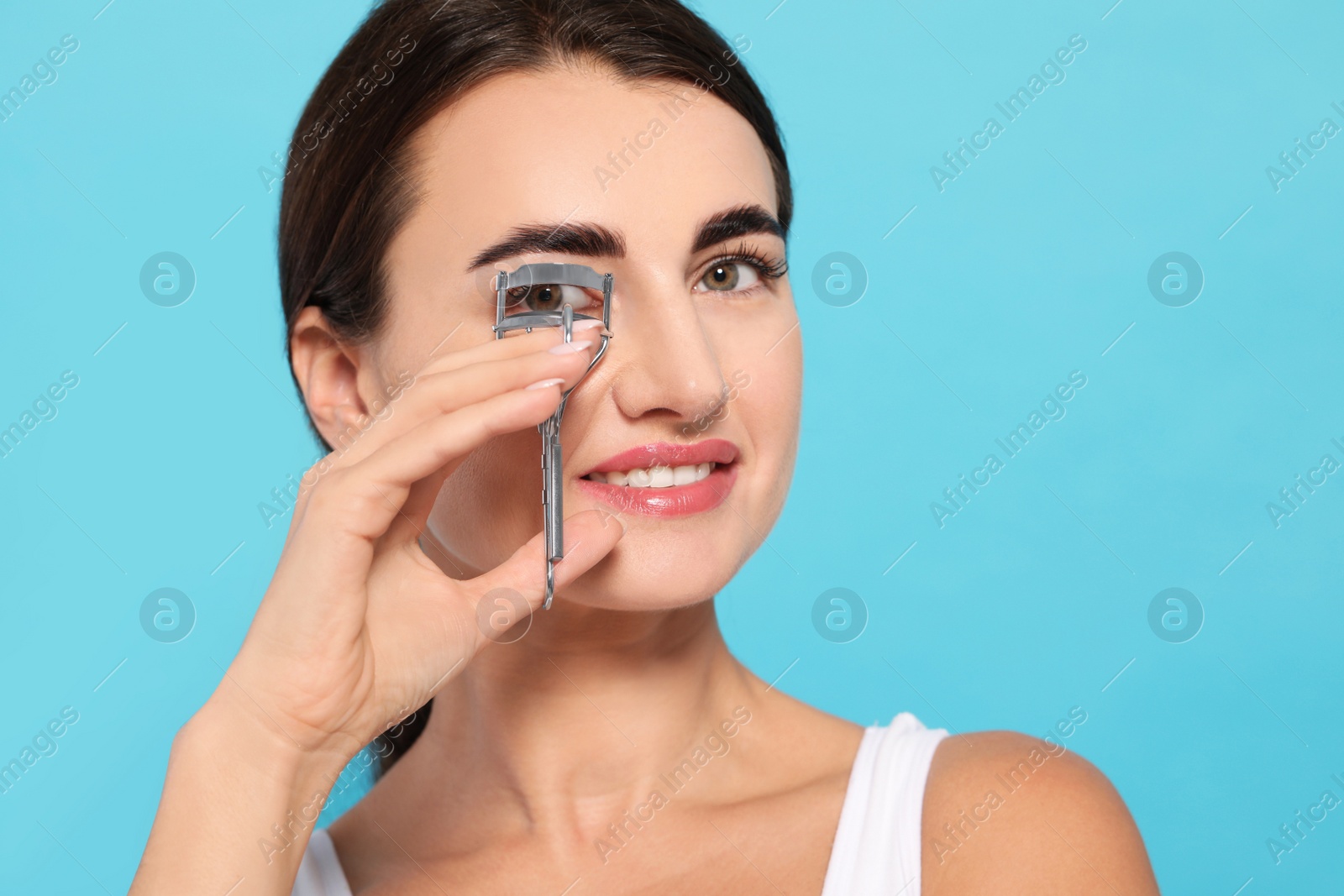 Photo of Woman using eyelash curler on turquoise background