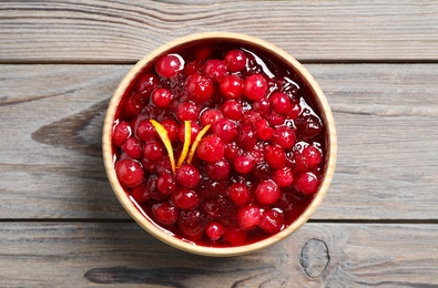 Photo of Fresh cranberry sauce with orange peel on wooden table, top view