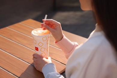 Photo of Lviv, Ukraine - September 26, 2023: Woman with McDonald's drink at wooden table outdoors, closeup
