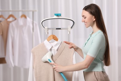 Woman steaming clothes on hanger at home