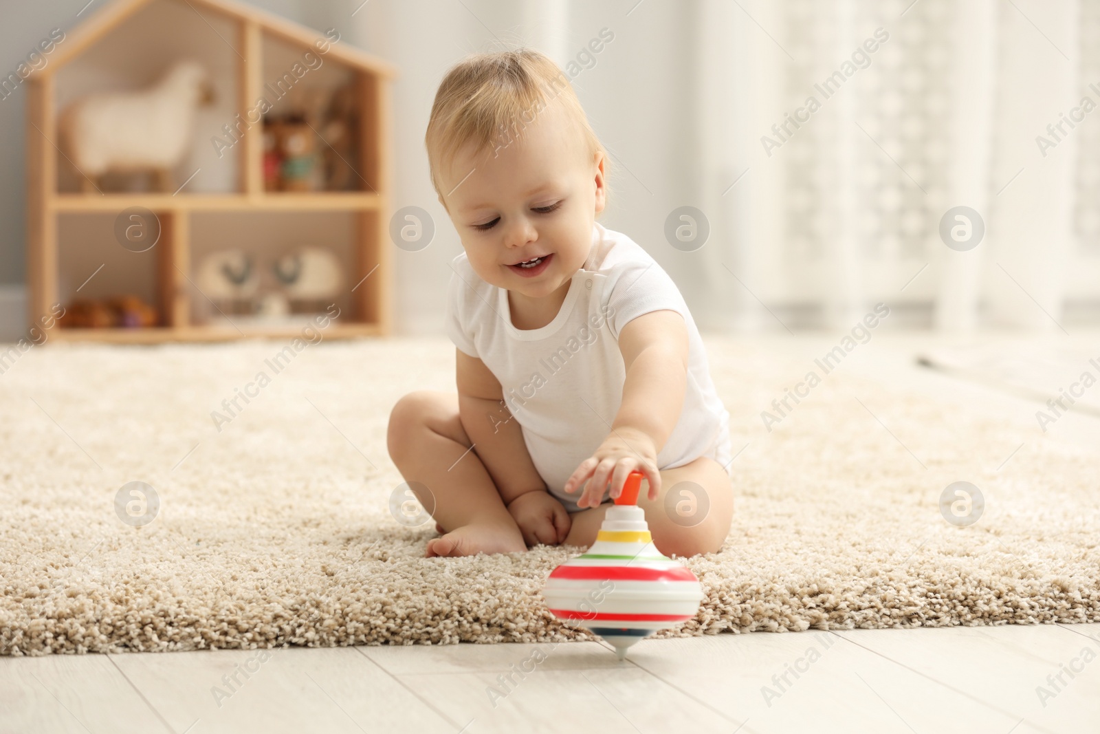 Photo of Children toys. Cute little boy playing with spinning top on rug at home