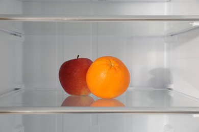 Apple and orange on shelf inside modern refrigerator