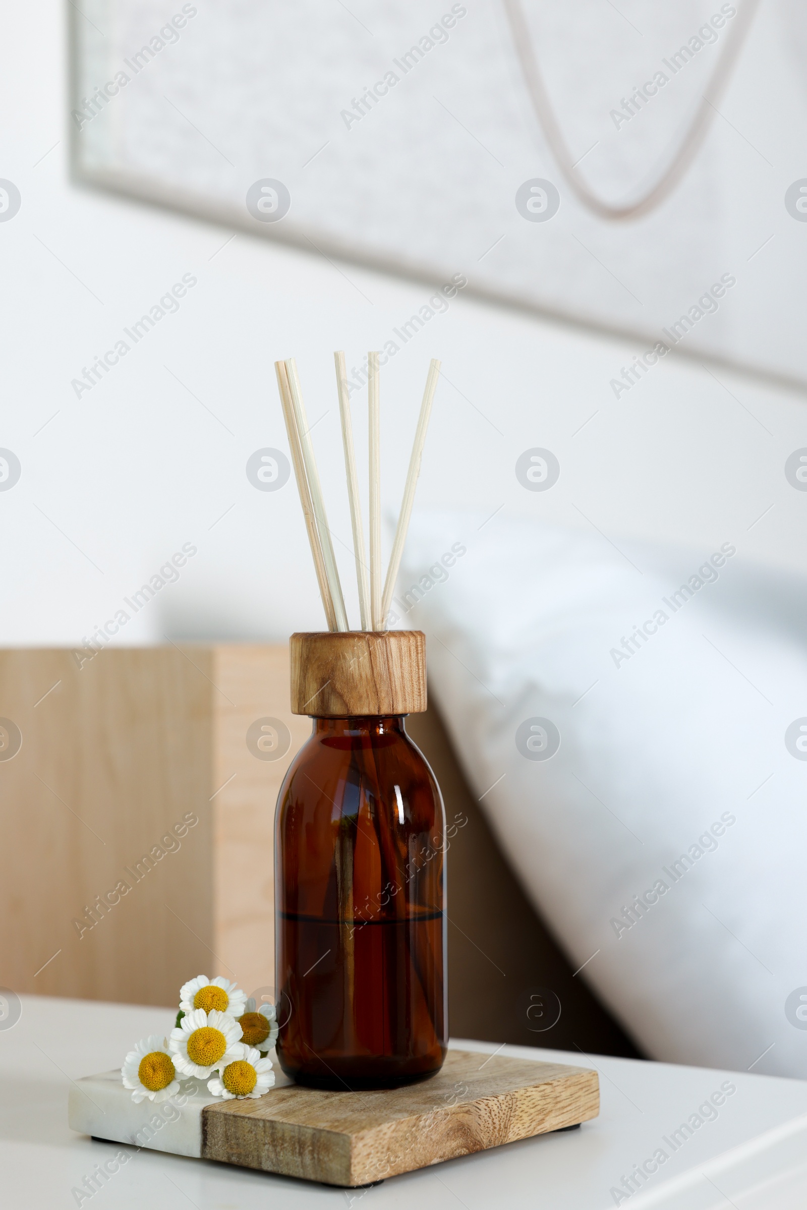 Photo of Aromatic reed air freshener and chamomiles on white nightstand in bedroom