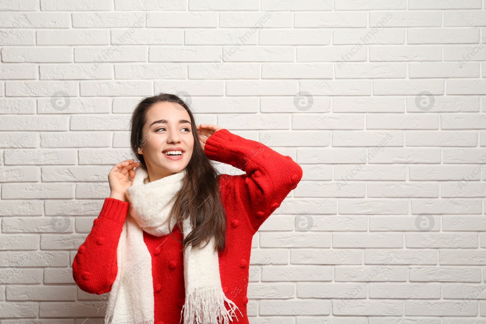 Photo of Young woman wearing warm clothes near brick wall, space for text. Winter season