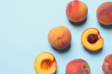 Photo of Cut and whole fresh ripe peaches on light blue background, flat lay. Space for text