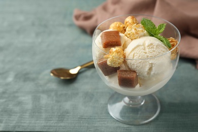 Photo of Delicious ice cream with caramel candies and popcorn in dessert bowl on blue wooden table. Space for text