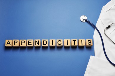 Photo of Word Appendicitis made of wooden cubes and doctor uniform with stethoscope on blue background, flat lay. Space for text