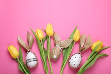 Photo of Easter bunnies made of craft paper and eggs among beautiful tulips on pink background, flat lay