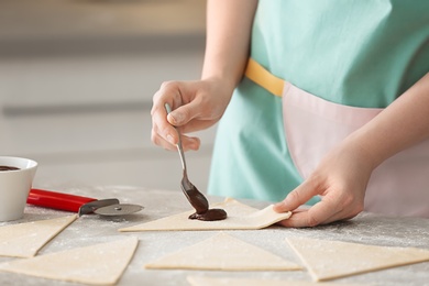 Photo of Woman preparing tasty croissants with chocolate paste on table, closeup