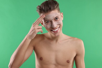 Handsome man applying facial mask onto his face on green background