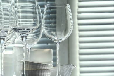 Photo of Set of empty wine glasses and dishware near window, closeup