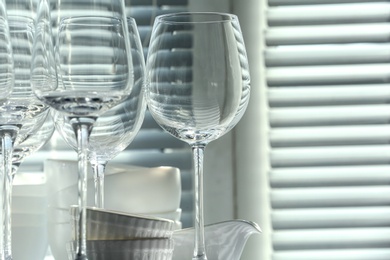 Set of empty wine glasses and dishware near window, closeup