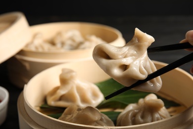 Photo of Woman cooking tasty baozi dumplings in bamboo steamer at table, closeup