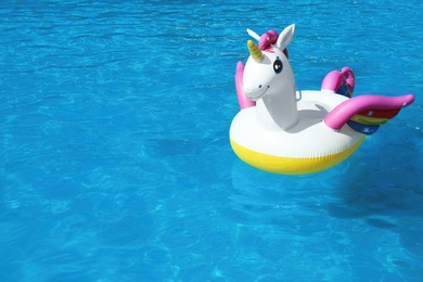 Photo of Funny inflatable unicorn ring floating in swimming pool on sunny day. Space for text