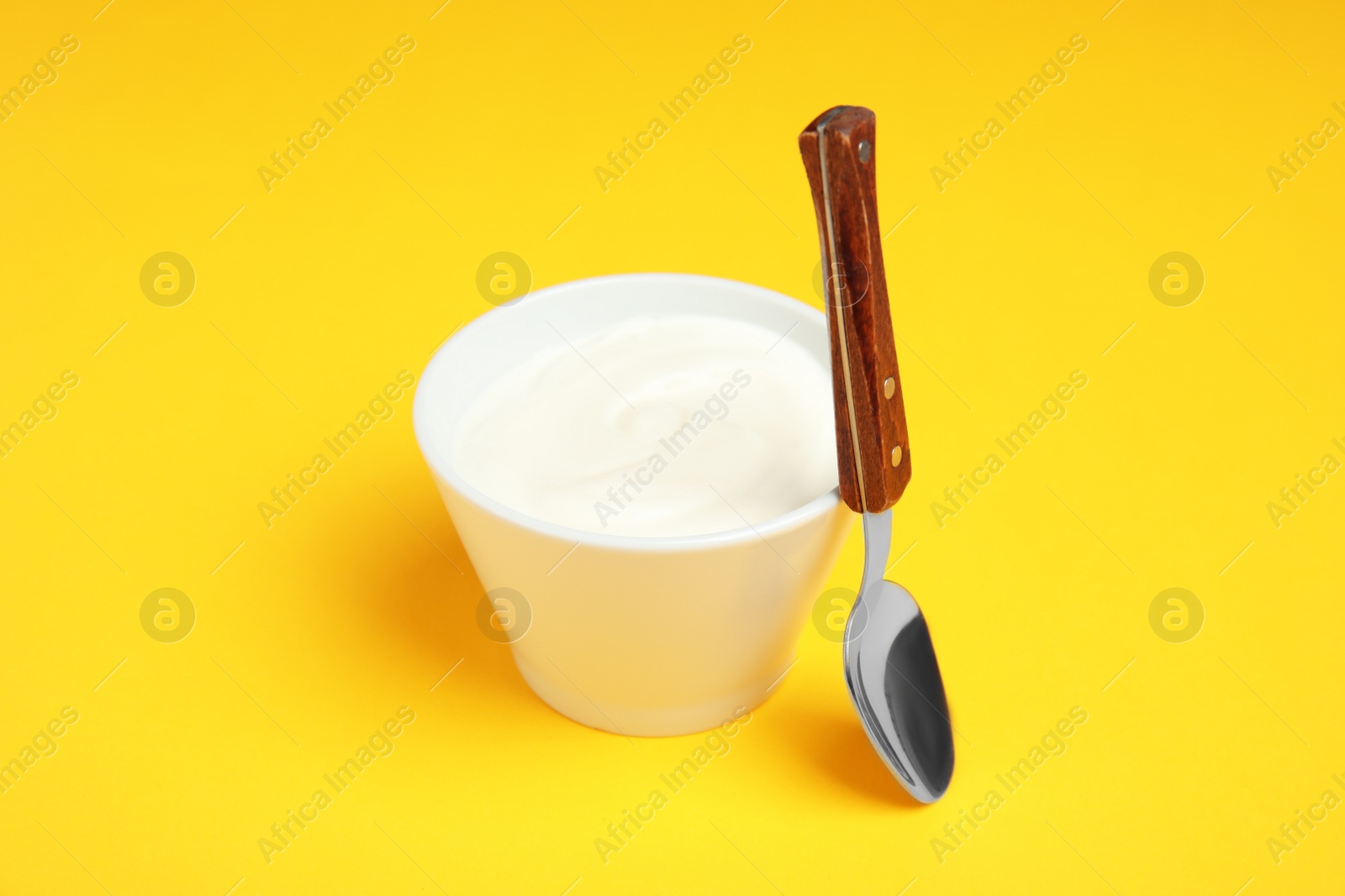 Photo of Bowl with creamy yogurt and spoon on color background