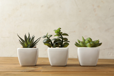 Photo of Artificial plants in white flower pots on wooden table