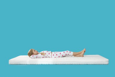 Little girl lying on comfortable mattress against light blue background, space for text