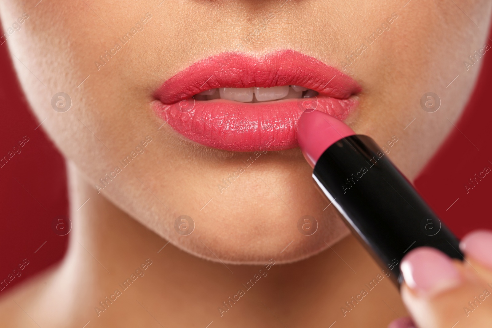 Photo of Young woman applying lipstick on color background, closeup