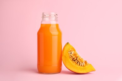 Photo of Tasty pumpkin juice in glass bottle and cut pumpkin on pink background