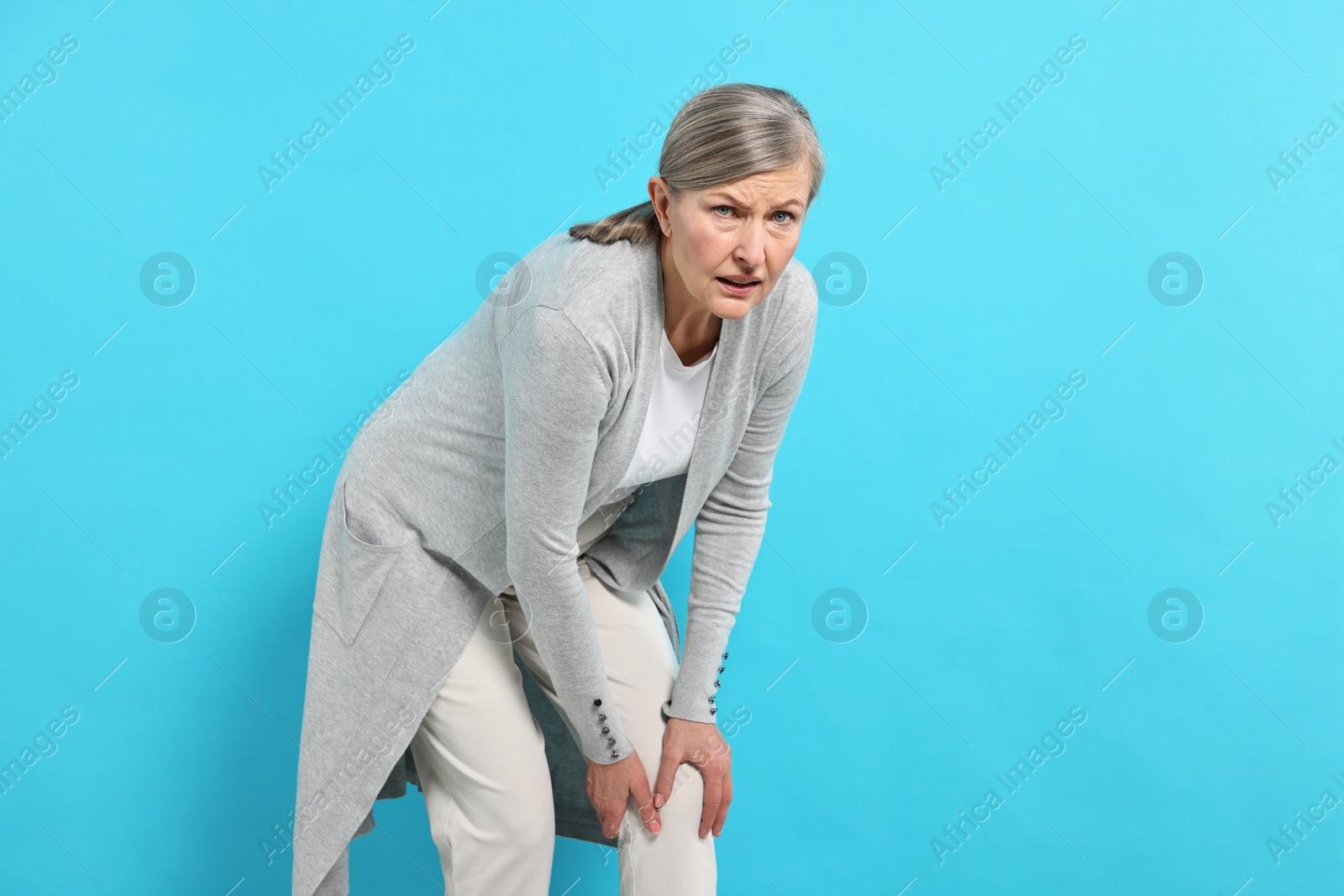 Photo of Arthritis symptoms. Woman suffering from pain in knee on light blue background