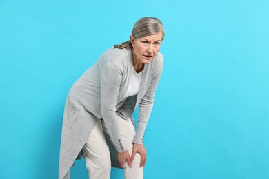 Photo of Arthritis symptoms. Woman suffering from pain in knee on light blue background