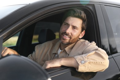 Photo of Enjoying trip. Happy bearded man driving his car, view from outside