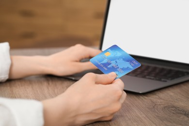 Photo of Woman with credit card using laptop for online shopping at wooden table indoors, closeup