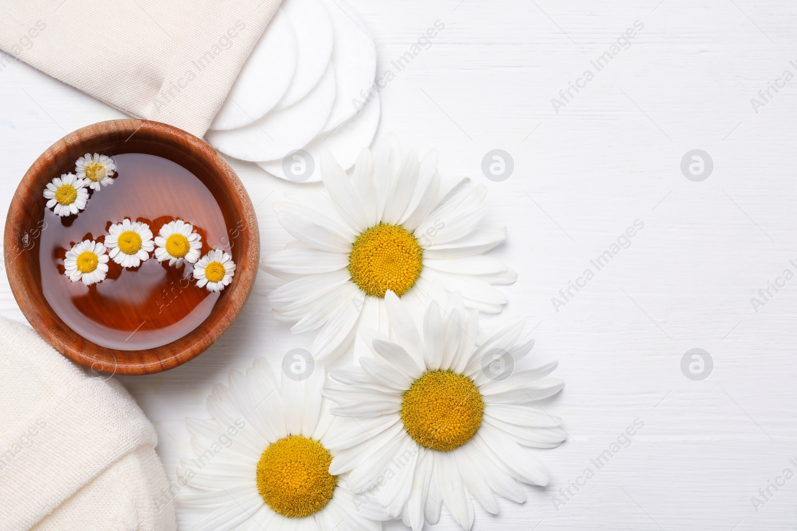 Photo of Flat lay composition with chamomile flowers and cosmetic product on white wooden table, space for text