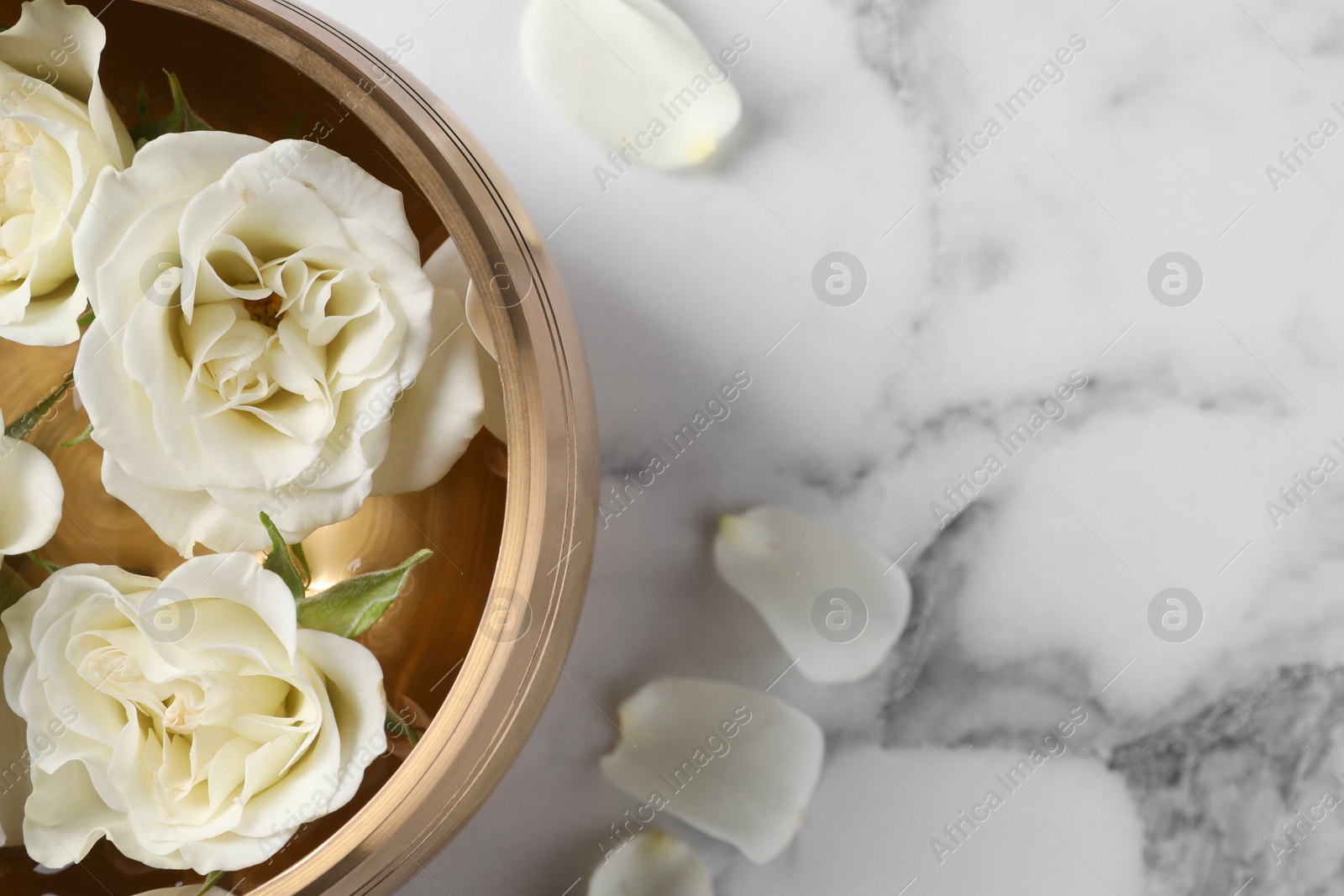 Photo of Tibetan singing bowl with water and beautiful roses on white marble table, top view. Space for text