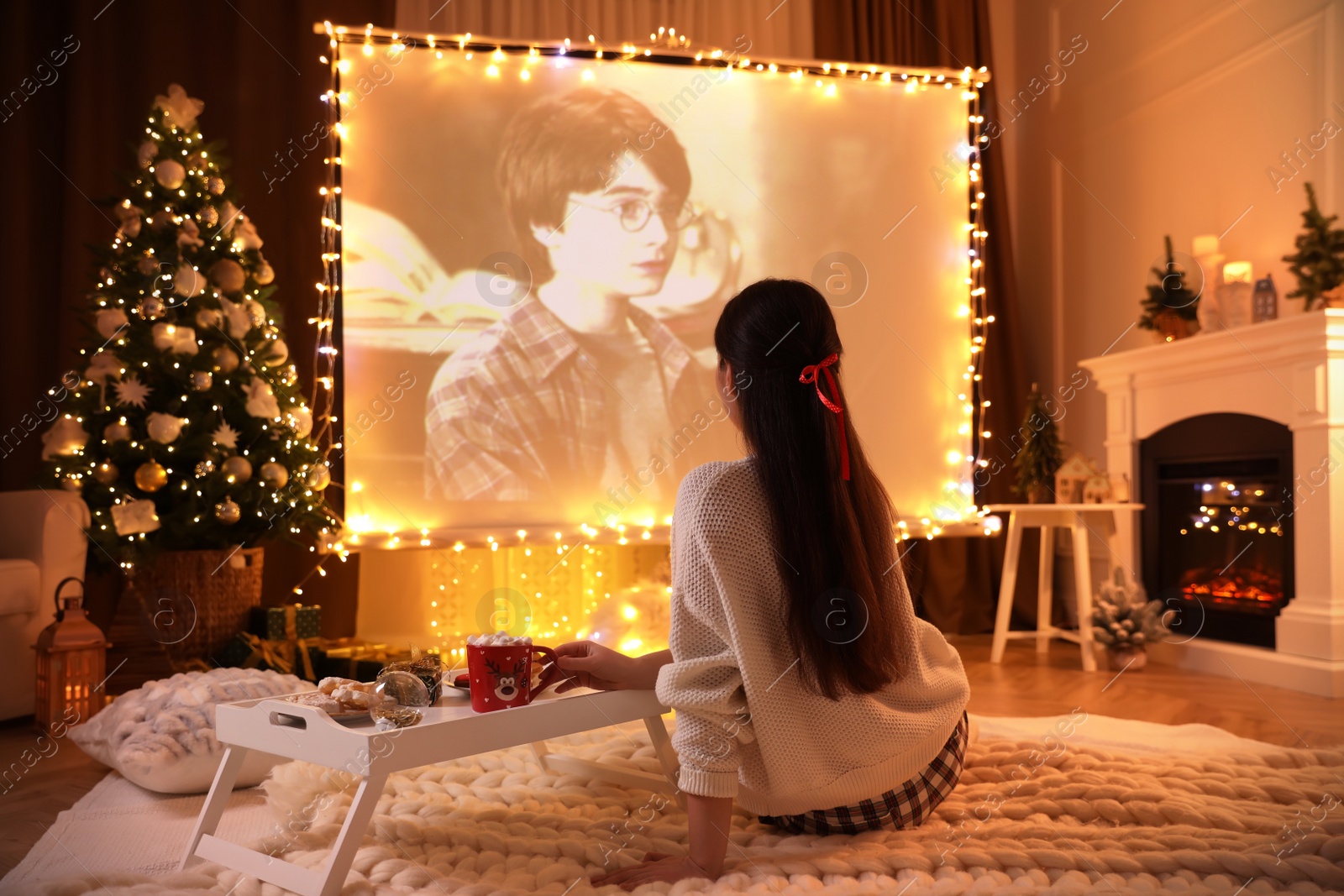 Photo of MYKOLAIV, UKRAINE - DECEMBER 24, 2020: Woman watching Harry Potter and Philosopher's Stone movie via video projector in room. Cozy winter holidays atmosphere