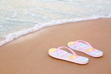 Photo of Stylish flip flops on sand near sea, space for text. Beach accessories