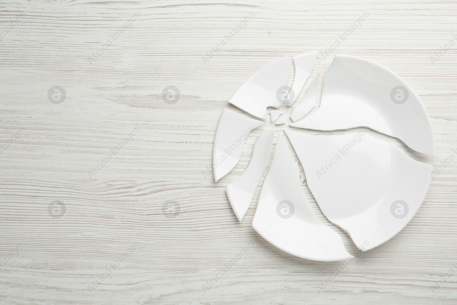 Photo of Pieces of broken ceramic plate on white wooden table, flat lay. Space for text